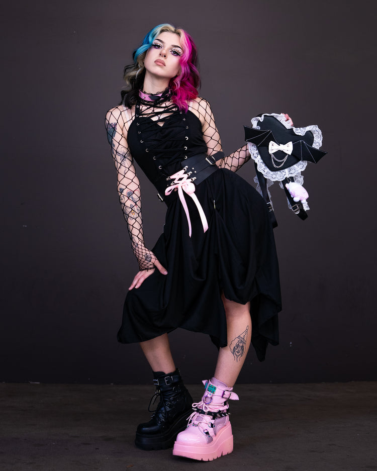 Model in an alternative fashion dress with pink and black split hair holding a matching themed parasol, showcasing gothic style.