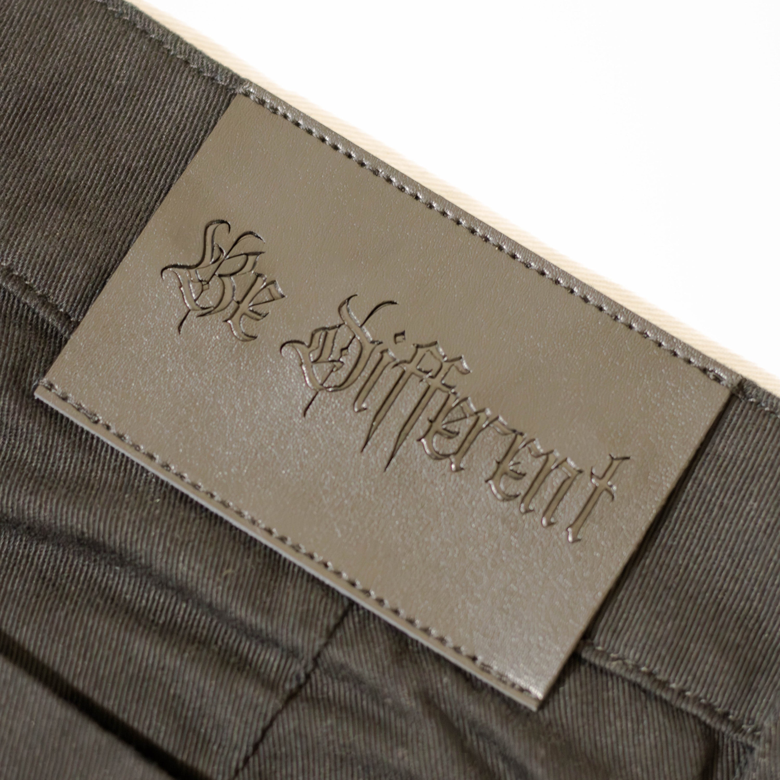 Close-up of a label reading 'Be Different' on a pair of trousers.